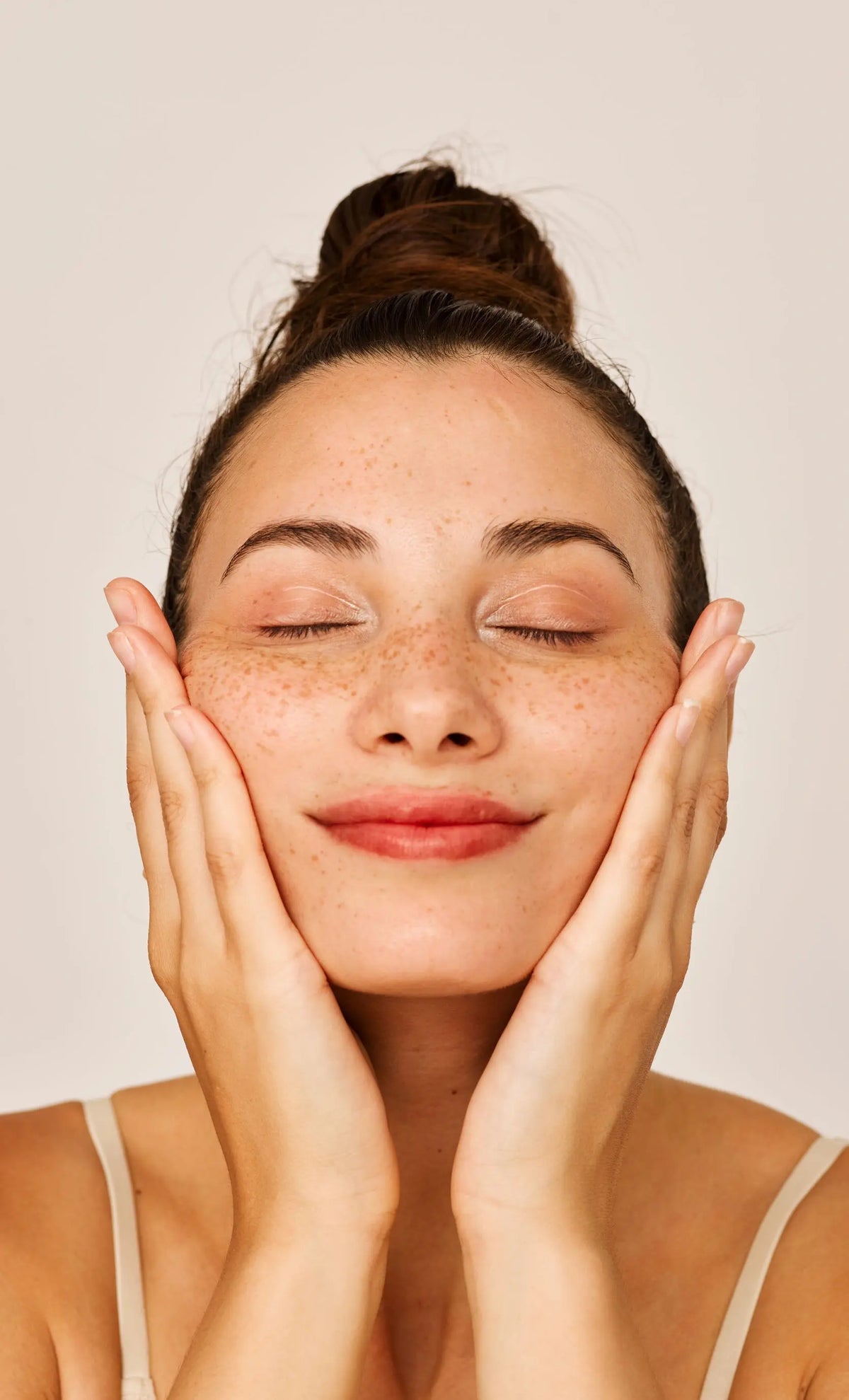 Close-up of a woman's face with her eyes closed, hands framing her cheeks