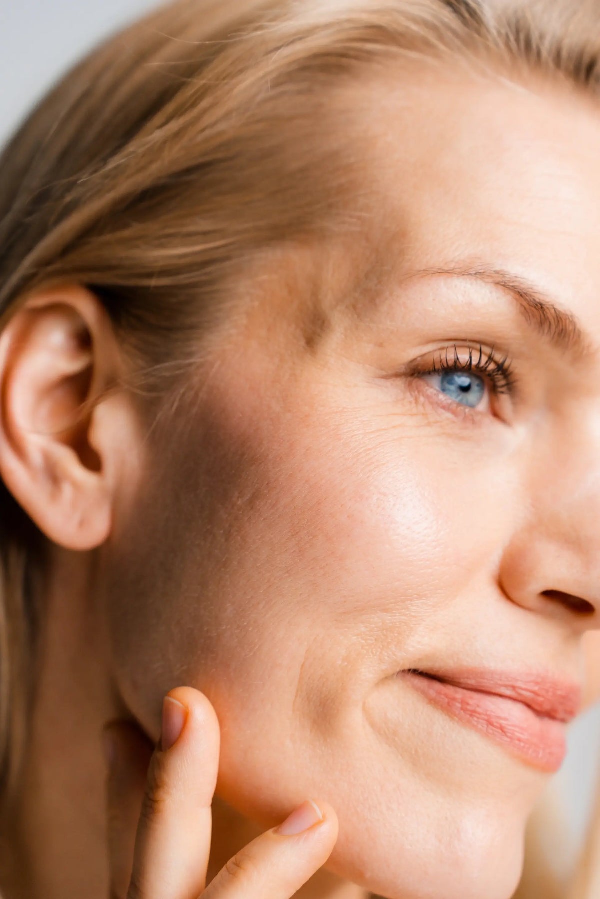 Close-up of a woman's face with blue eyes, touching her cheek