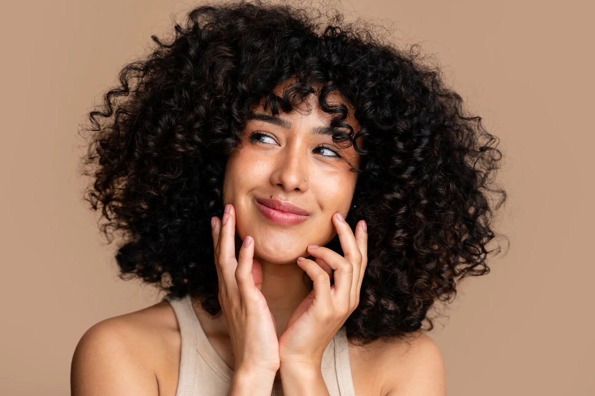 Woman with curly hair smiling, hands framing her jawline